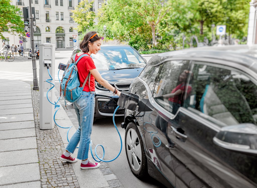 Woman charging her electro car at special parking, alternative energy and eco concept